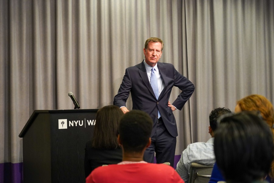 Bill de Blasio wears a light navy suit while standing next to an N.Y.U. Wagner podium, during the question-and-answer portion of an event he was appearing at.